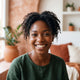 Close-up portrait of a smiling woman in her late 20s, exuding confidence and happiness, against a warm background.